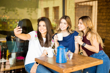 Good looking female friends taking selfie at cafe