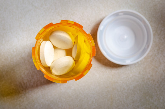 Above View Of Pills In An Open Yellow Pill Bottle And Lid