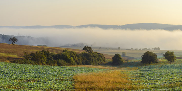 Countryside with morning mist over the fields in Grossheubach with the Spessart hills in the background in Bavaria, Germany