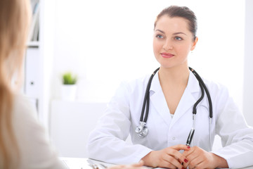 Brunette female doctor talking to patient at hospital office. Physician says about medical exams results for choosing optimal treatment. Healthcare and medicine concept