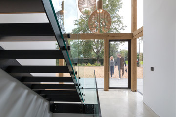 Couple arriving home viewed through glass entrance from modern staircase.