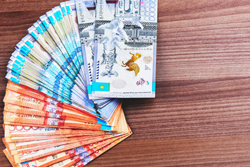 Tenge. A lot of Kazakh banknotes are laid out on a brown wooden table close-up..
