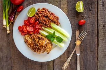 Healthy food. Plate with fried chicken, wheat grains, tomatoes, cucumber and lime on wooden background.