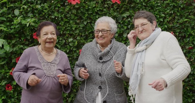 portrait of diverse elderly women dancing happy enjoying celebrating retirement listening to music together in outdoors garden