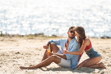 couple with cocktails sitting on beach near the sea in summer