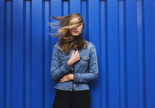 Blond girl posing against blue wall in wind