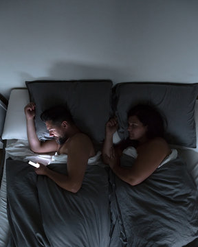 Couple using their phones in bed at night