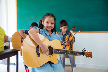 Pretty asian girl smiling with guitar in school classroom.