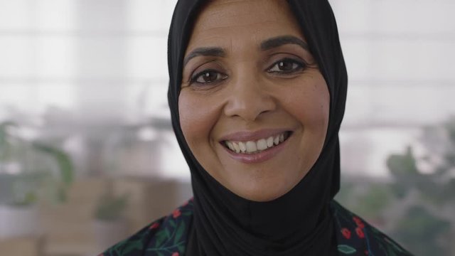 close up portrait of senior muslim business woman smiling looking cheerful at camera wearing traditional headscarf mature experienced female in office workspace