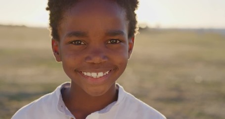 close up portrait of cute african american boy smiling cheerful looking at camera happy enjoying sunny day at seaside park bright vibrant sunset - Powered by Adobe