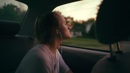 Young girl longingly looks out window of car at dusk
