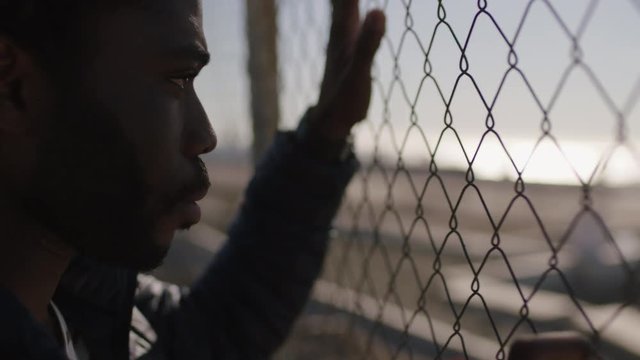 close up portrait of young african american man looking unhappy disappointed hands holding fence depressed frustrated black male