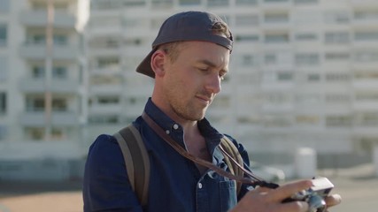 portrait of attractive young photographer man taking photo using retro camera technology wearing relaxed fashion on warm sunny urban day