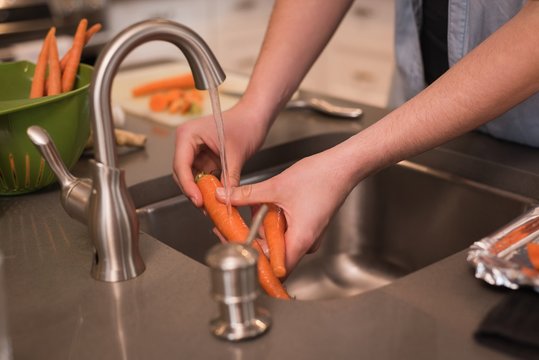 Woman washing carrot in kitchen at home