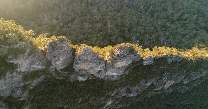 Three rocks dubbed Three Sisters in Blue Mountains of Australia at sunrise. Aerial overhead flying from above natural landmark lit by warm morning light.
