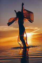 Fototapeta premium beautiful young woman in elegant dress walking on water at sunset