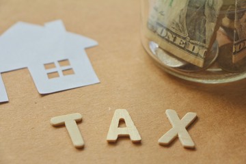 Paper cut of house with money in jar,text tax wood.