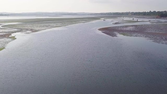Drone flying over the beautiful beach of Lympstone England. Docked boats can be seen in the distance, as well as hills and mountains.