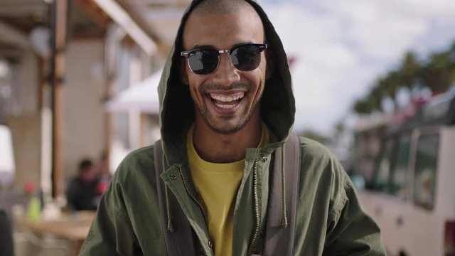 portrait of handsome hispanic man laughing happy on sunny beachfront wearing hoodie