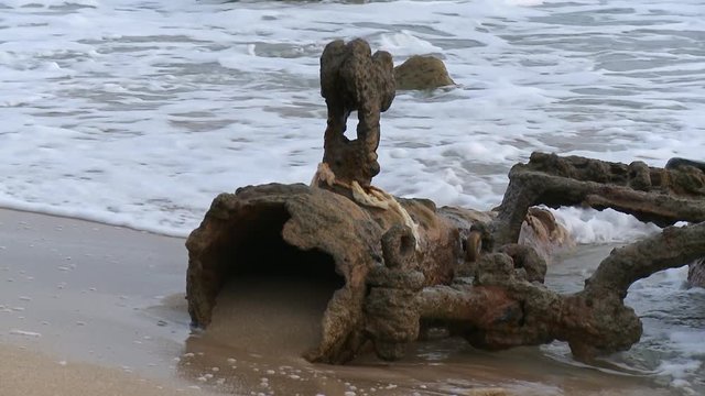 Close up of a ship wreck&rsquo;s corroded debris on a sandy beach, surrounded by calm waves