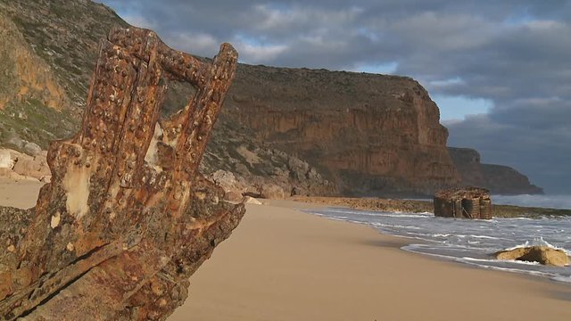 Corroded pieces of a ship wreck on a sunny, sandy beach with calm surf in the afternoon sunlight and