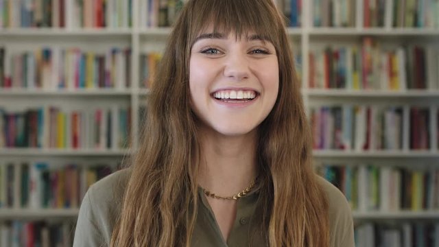 close up portrait of young happy caucasian woman laughing cheerful cute librarian in library bookshelf background