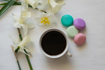 Morning coffee, macaron and daffodils on a white board. Composition of a bouquet of daffodils and cups of coffee.