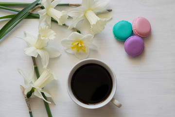 Morning coffee, macaron and daffodils on a white board. Composition of a bouquet of daffodils and cups of coffee.