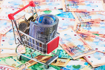 Tenge. A pack of Kazakh banknotes in a shopping cart on the background of a pile of money. Close up..
