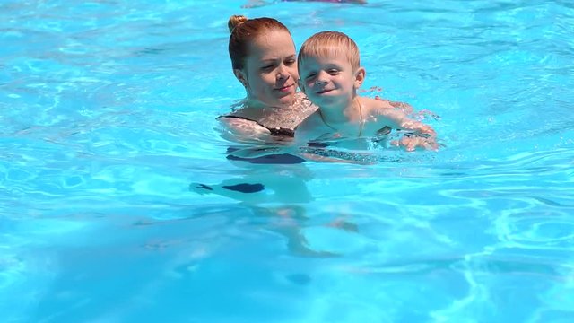 A young mother teaches her little son to swim in the pool in the summer on vacation. Happy little boy swimming in pool with mom. Slow motion.