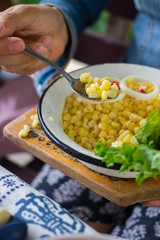Woman hands holds sweet white corn or yellow corn cooked. Tasting grains cut into metal bowl. Vegetarian lunch. Vegan dinner. Healthy food. Served with green salad leaves.