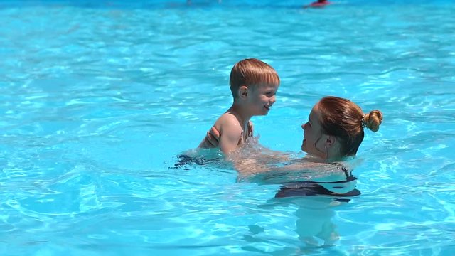 A cheerful family, a young mother with her son, have fun and play in the pool. They bathe, sunbathe and enjoy the hot weather in the hotel at the resort.