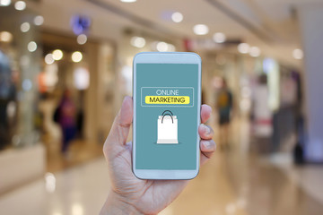 Hand holding smartphone with  text ONLINE MARKETING on screen over blurred in shopping mall background