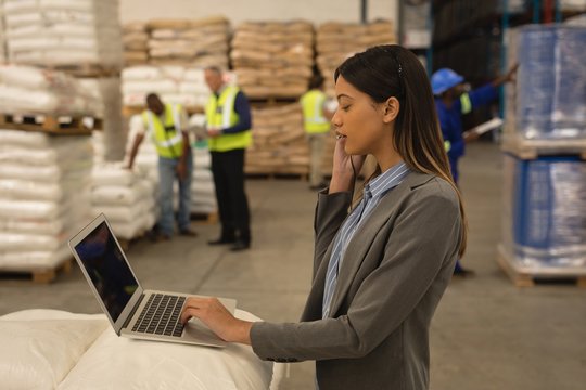 Female supervisor talking on mobile phone while using laptop