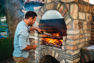 Summertime fun. Young man cooking meat on a brick barbecue.