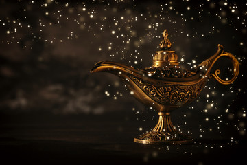 Image of magical mysterious aladdin lamp with glowing glitter lights over black background. Lamp of...