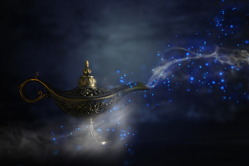 Image of magical mysterious aladdin lamp with glitter sparkle smoke over black background. Lamp of...