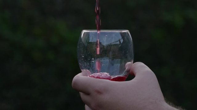 SLOW MOTION FOOTAGE pouring red drink into glass with blurred moving background