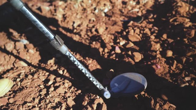 Metal Detector being held over exposed rocks by a geologist to look for gold