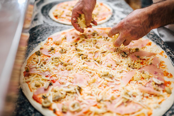 Chef adding cheese on unbaked pizza. Close-up.