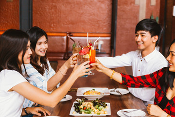 Group of Asian happy and smiling young man and women holding an alcoholic cocktail for toasting and celebrating in social party in restaurant.