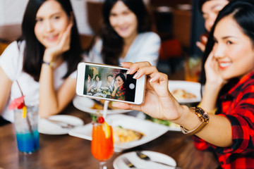 Group of Happy Asian male and female friends taking a selfie photo and having a social toast together in restaurant.