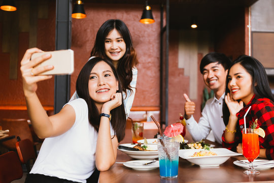 Group of Happy Asian male and female friends taking a selfie photo and having a social toast together in restaurant.
