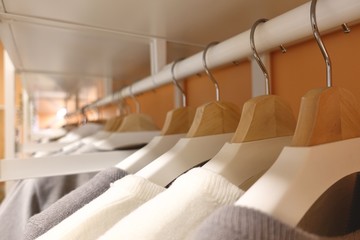 modern wooden wardrobe with clothes hanging on rail in walk in closet, Choice of fashion clothes of different colors on wooden hangers