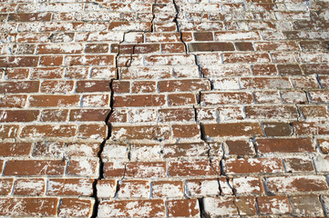 Part of the red brick wall of an old house with figured cracks due to the destruction of the Foundation. Background