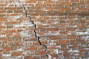 Part of the red brick wall of an old house with figured cracks due to the destruction of the Foundation. Background