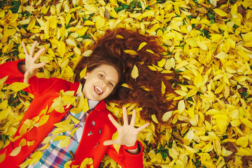 Beautiful happy girl laying in yellow autumn leaves.