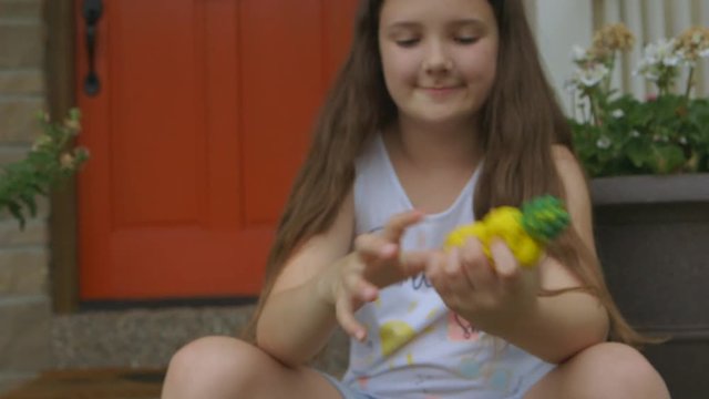 cute little girl sits on the porch and smiles at camera holding a pineapple squishy