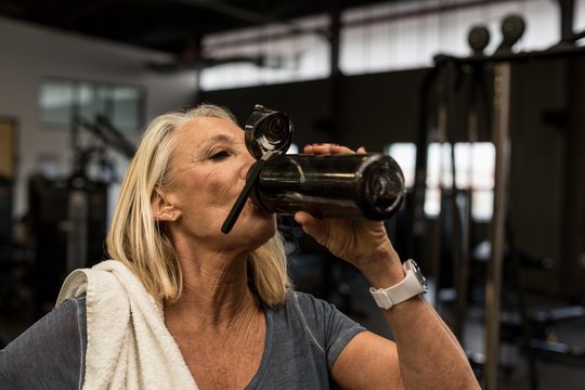 Mature woman drinking water in the gym