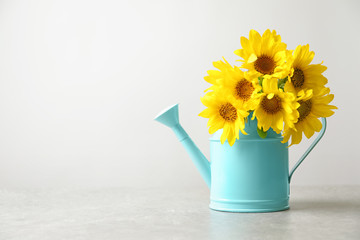 Watering can with beautiful yellow sunflowers on table